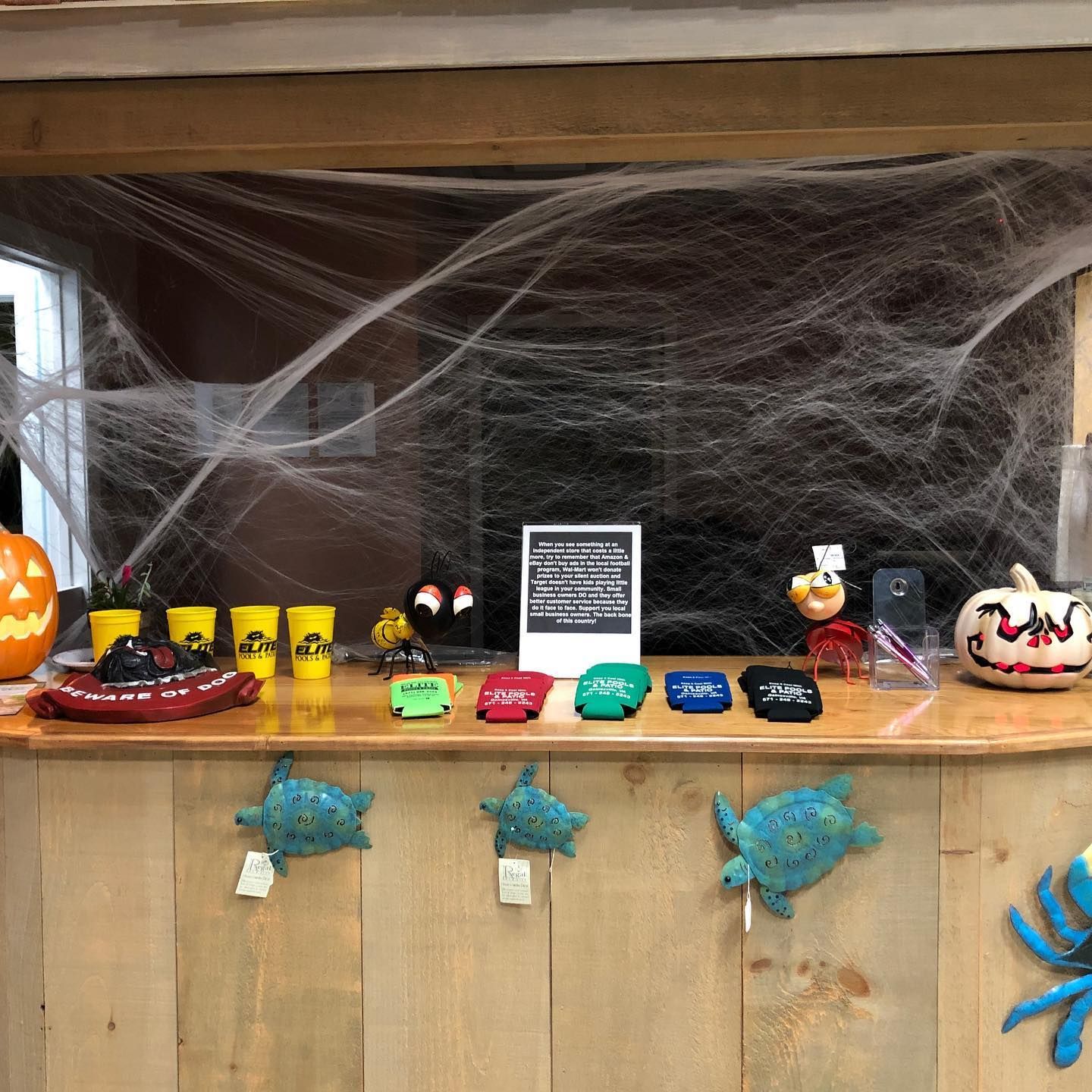 Halloween display with pumpkins, cups, figurines, and faux cobwebs on a wooden counter.