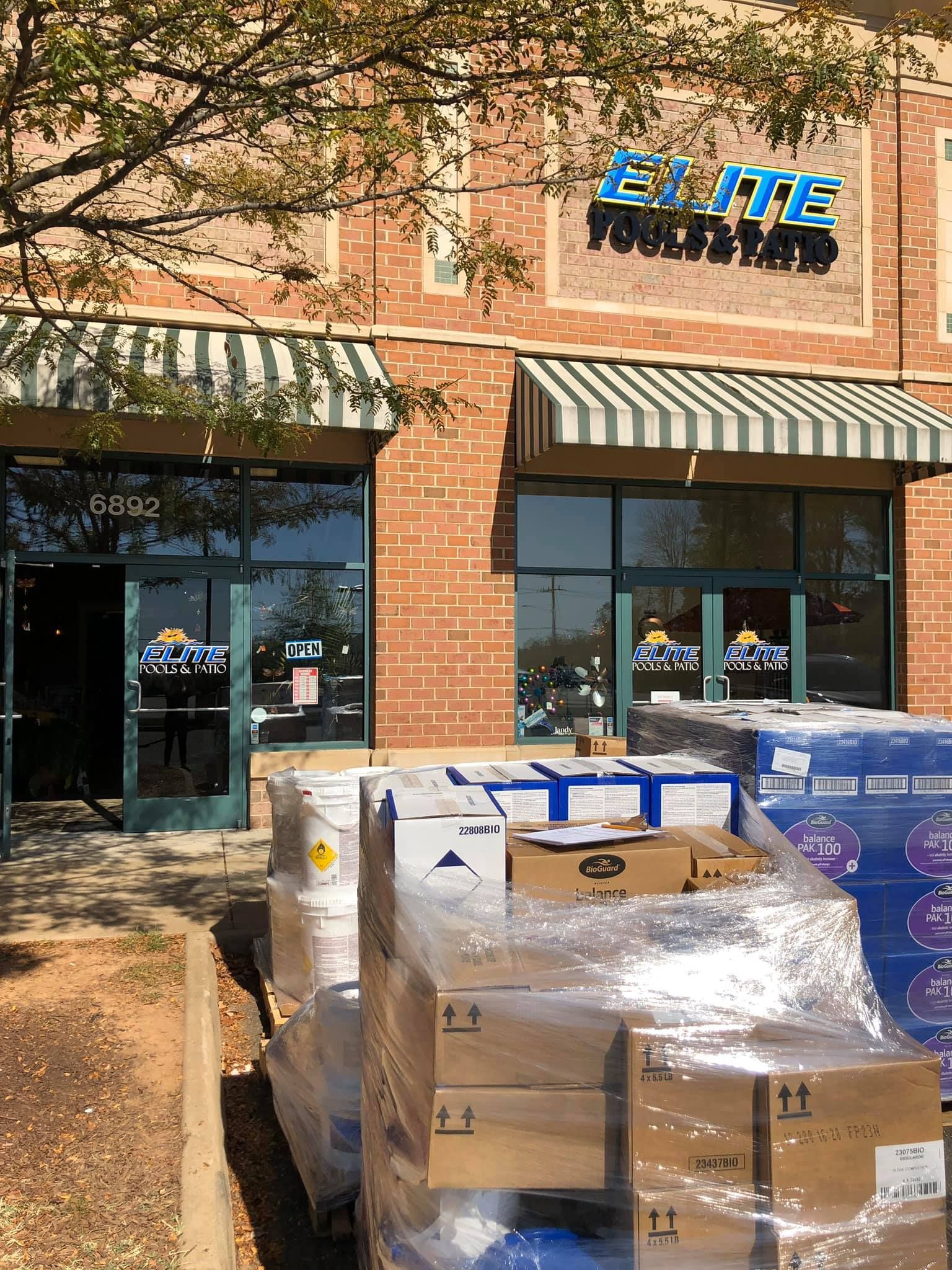 Exterior of a store with a green and white striped awning. Boxes wrapped in plastic are stacked in front.