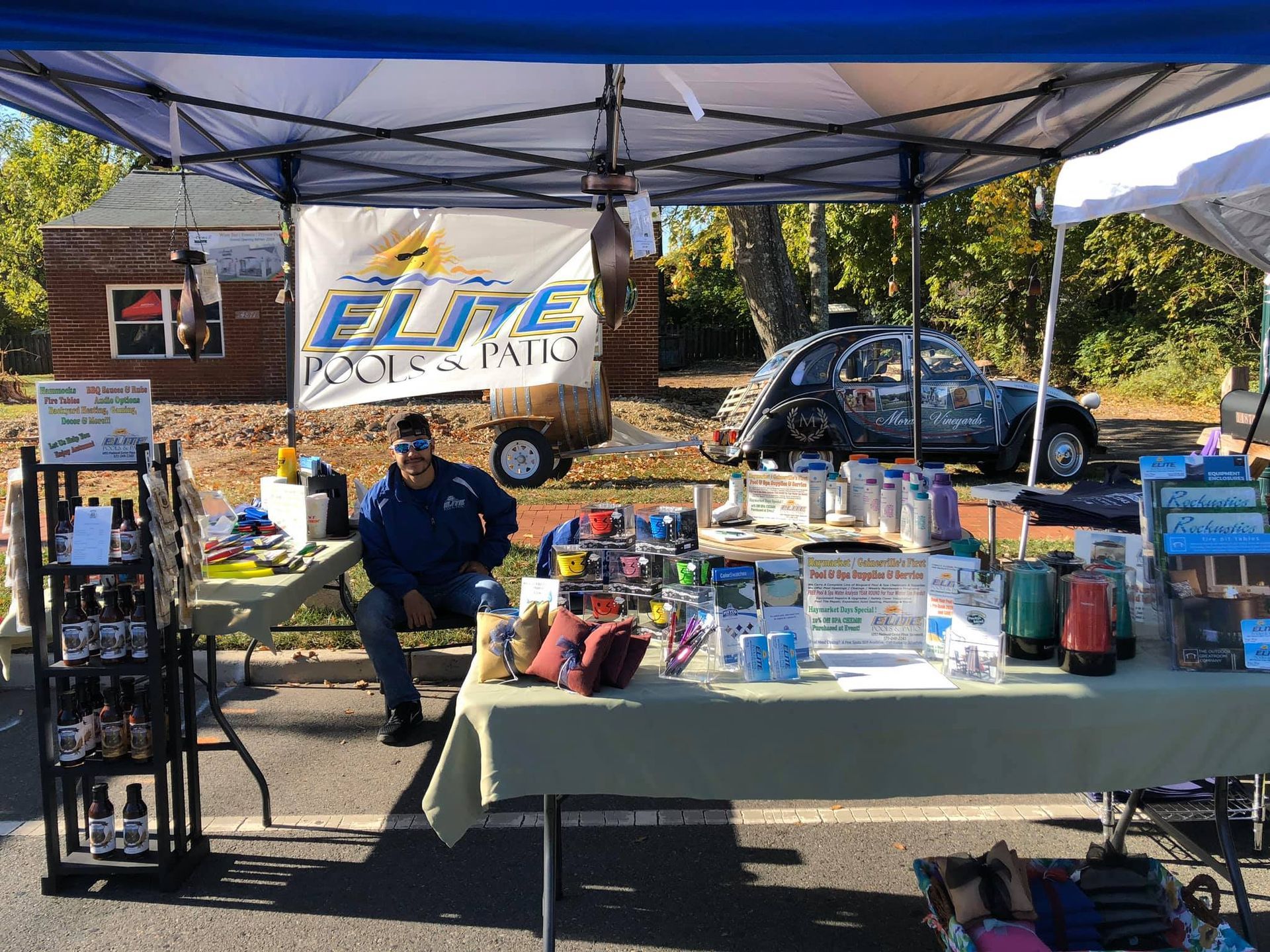 A vendor sits at a market stall selling goods under a blue canopy. A banner reads 