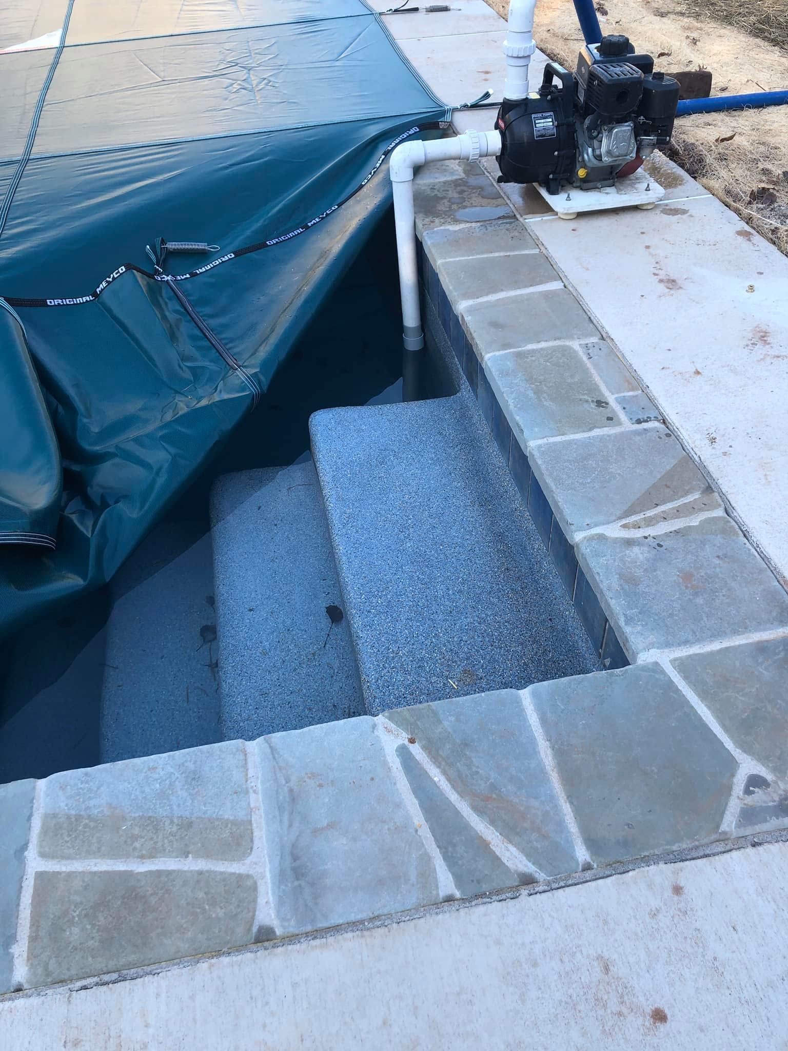 Pool steps with textured surface, next to a concrete border. A pump sits on the side.