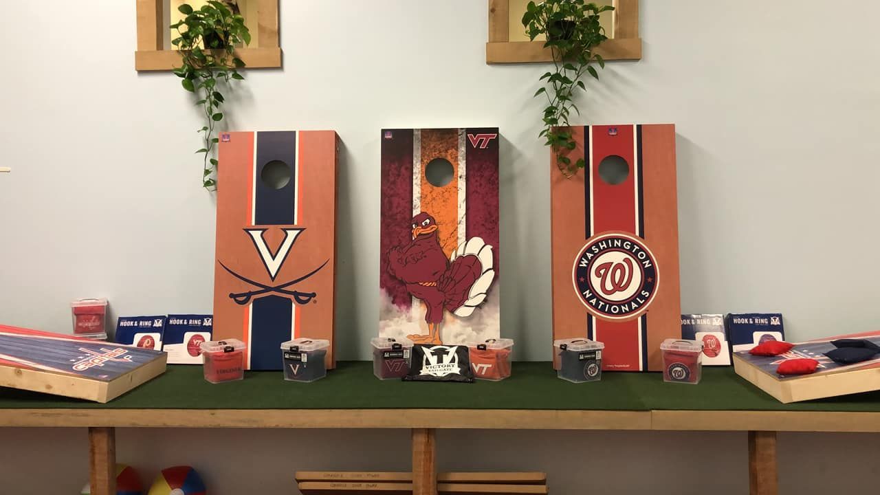 Three cornhole boards with sports team logos and bean bags on a green mat.