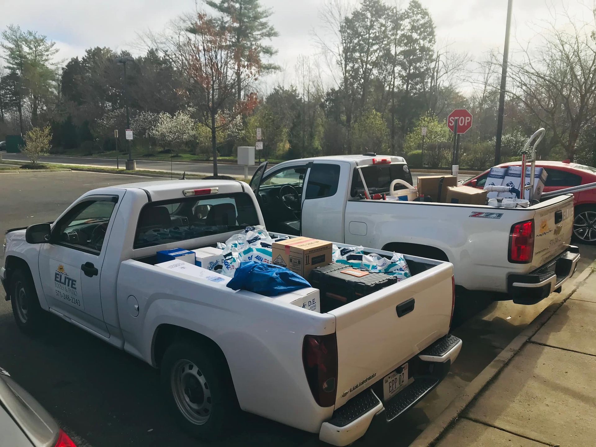 Two white pickup trucks loaded with supplies parked outdoors, near trees and a stop sign.