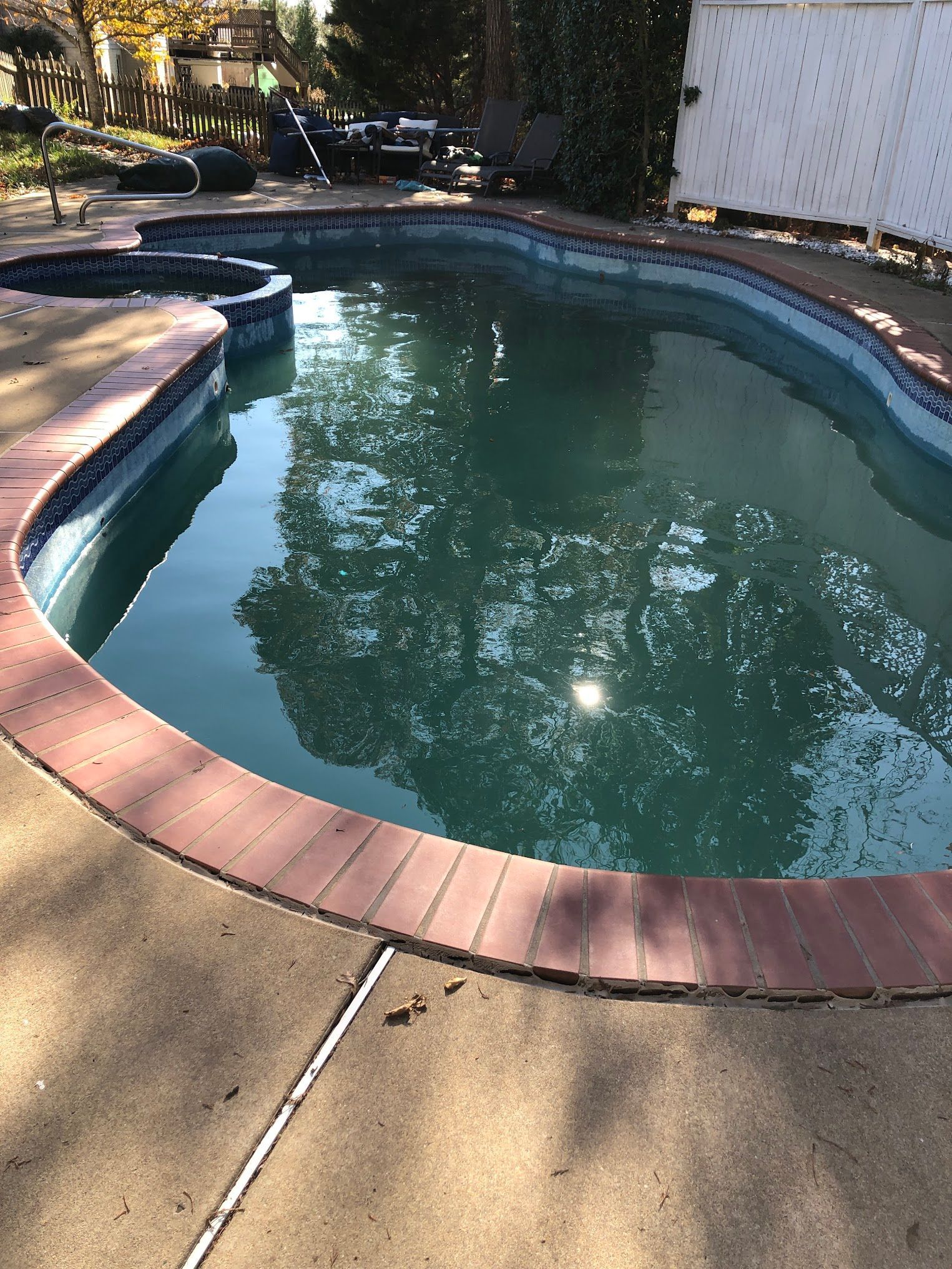 Pool with turquoise water, surrounded by a brick border and concrete deck. A spa is adjacent.