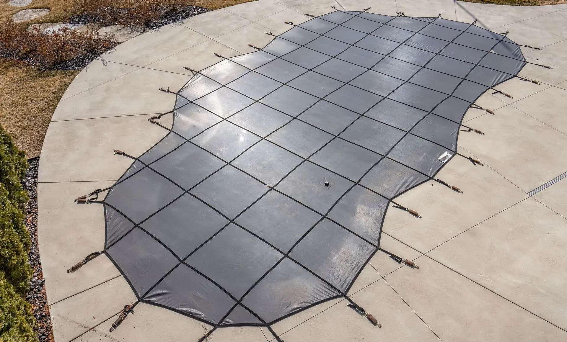 Black pool cover stretched over a concrete surface.