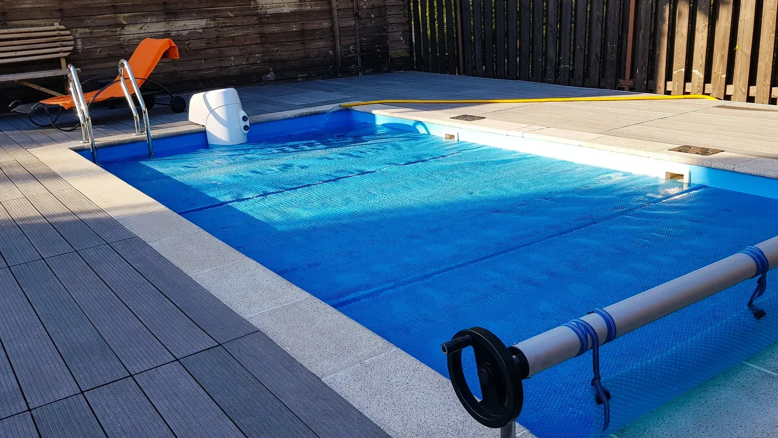 Small rectangular pool with blue cover, surrounded by grey decking and a wooden fence.