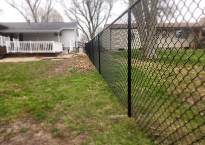 A chain link fence surrounds a lush green yard in front of a house.