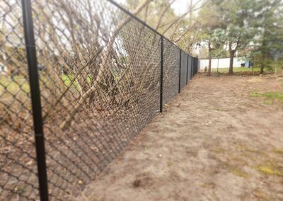 A chain link fence is surrounding a dirt field.