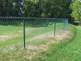 A chain link fence surrounds a grassy field in a park.