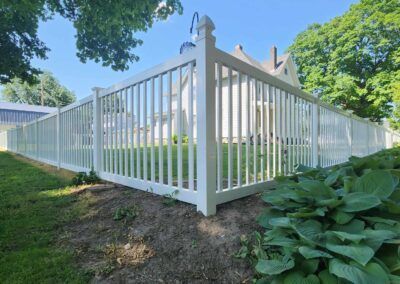 A white vinyl fence is surrounding a house in a backyard.