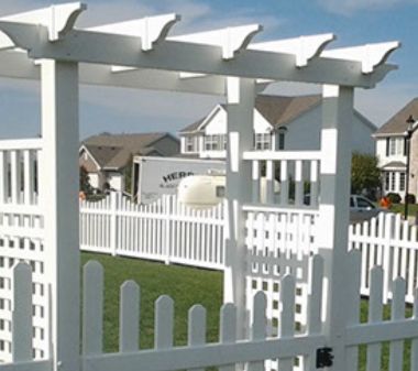 A white picket fence with a pergola in the background