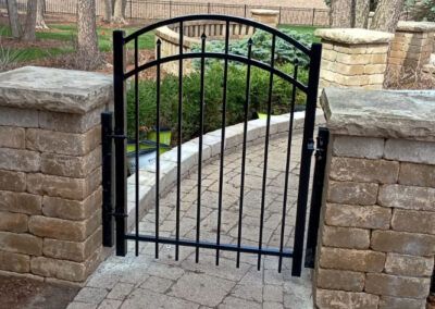A black gate is sitting next to a brick wall.