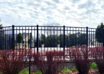 A black metal fence surrounds a swimming pool in a residential area.