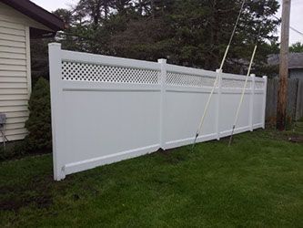 A white vinyl fence is sitting in the grass in front of a house.
