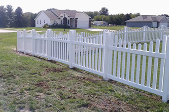 A white picket fence surrounds a lush green field in front of a house.