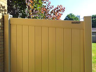 A yellow wooden fence is sitting next to a brick building.