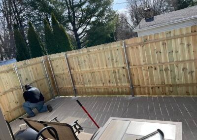 A man is kneeling on a deck next to a wooden fence.