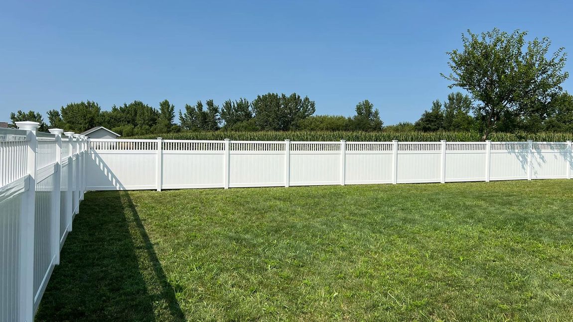 A white fence surrounds a large lush green field.