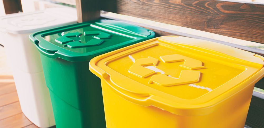 Six green trash bins lined up on a sidewalk.