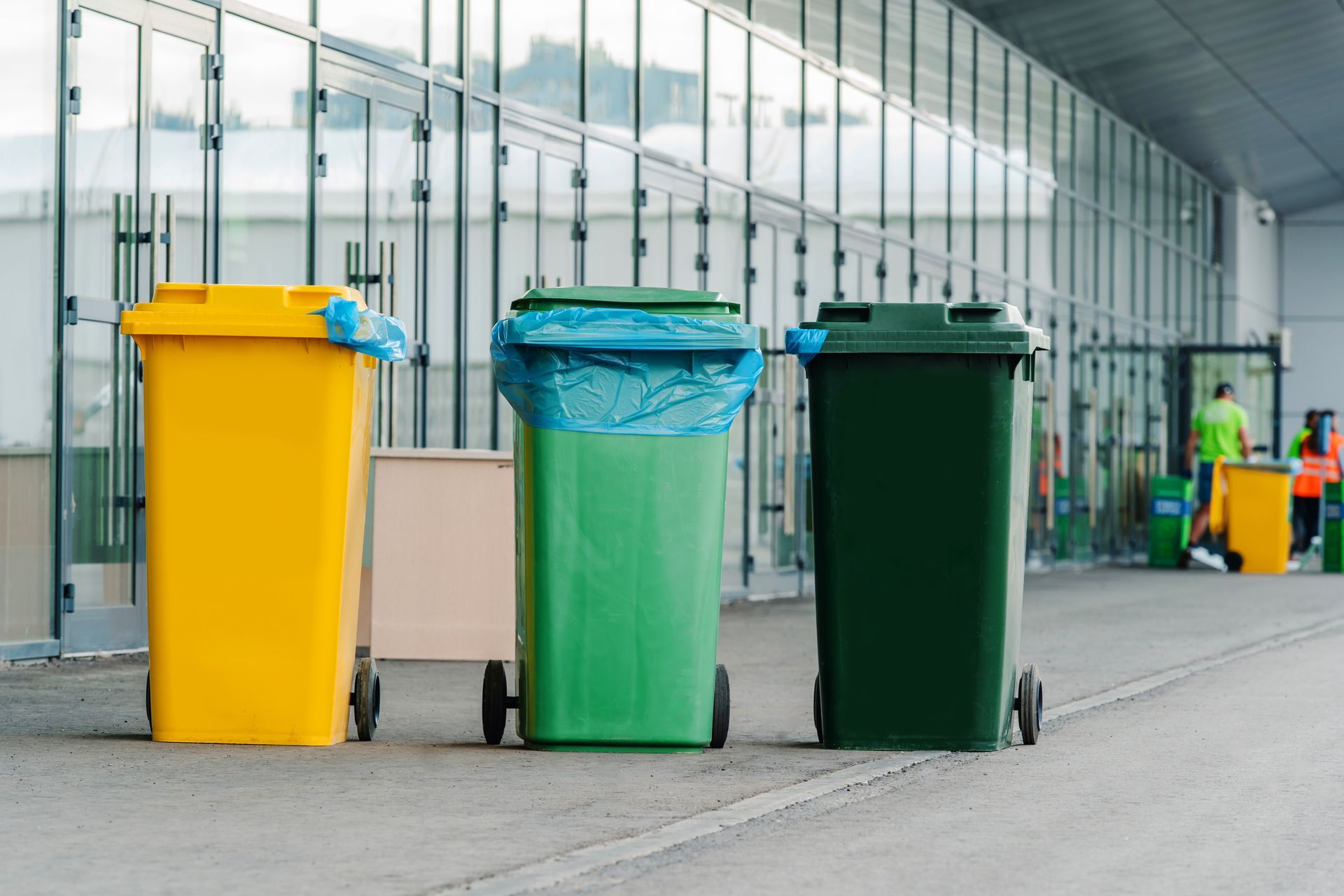 Six green trash bins lined up on a sidewalk.