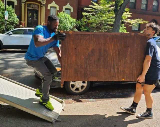 Two people are carrying a large wooden box on a ramp.