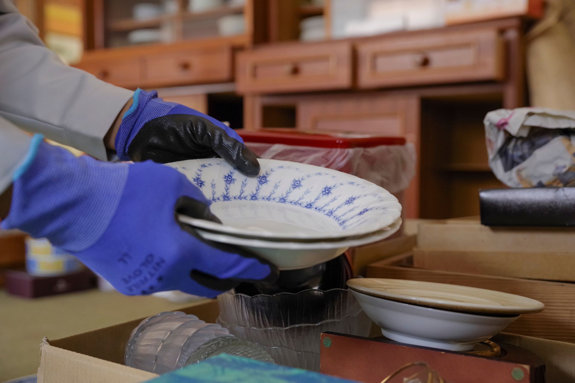 Hands in blue gloves holding two white plates with blue floral design, packing dishes into a box.