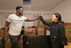 Two movers high-five in a room with cardboard boxes and moving equipment