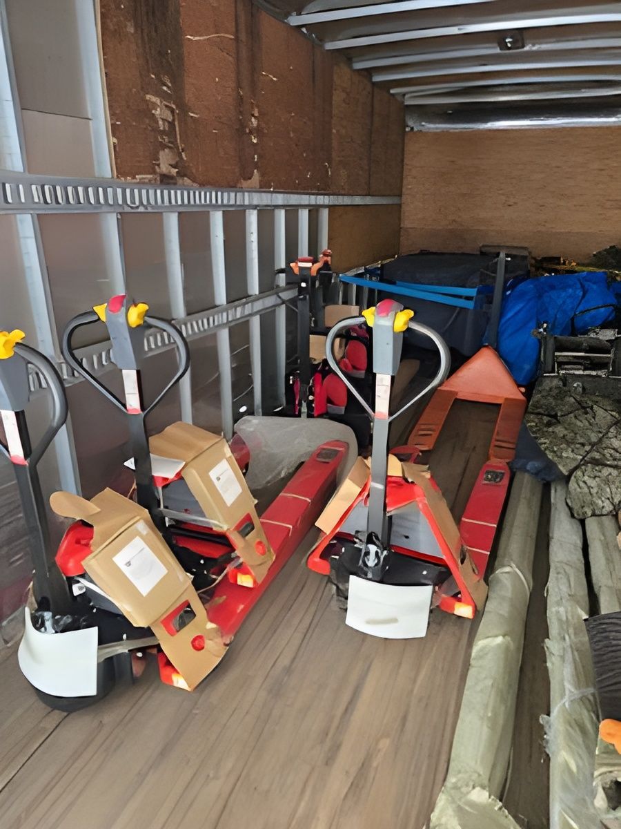 Two red and silver pallet jacks inside a cargo trailer.