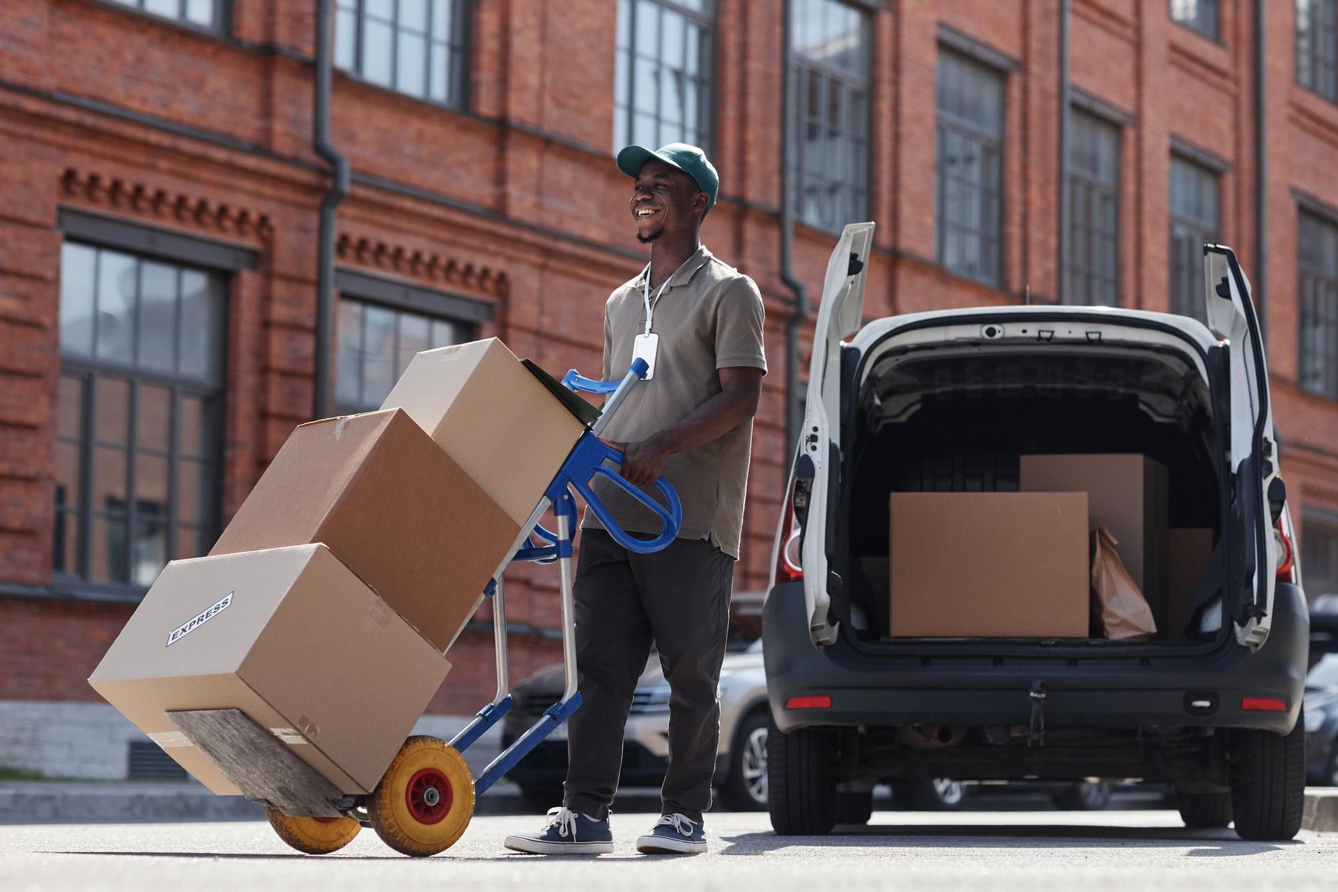 A delivery man is pushing a cart full of boxes next to a van.