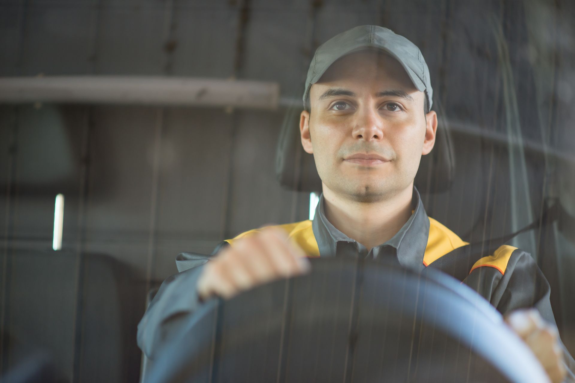 A man is driving a truck and looking at the camera through the windshield.