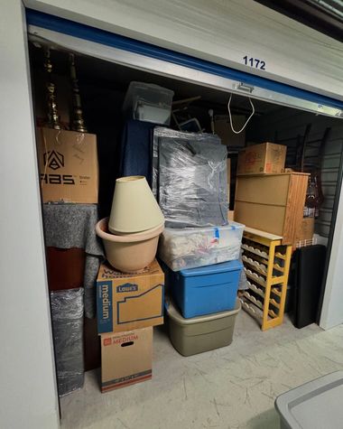 Storage unit packed with stacked boxes, bins, and wrapped furniture on the floor.
