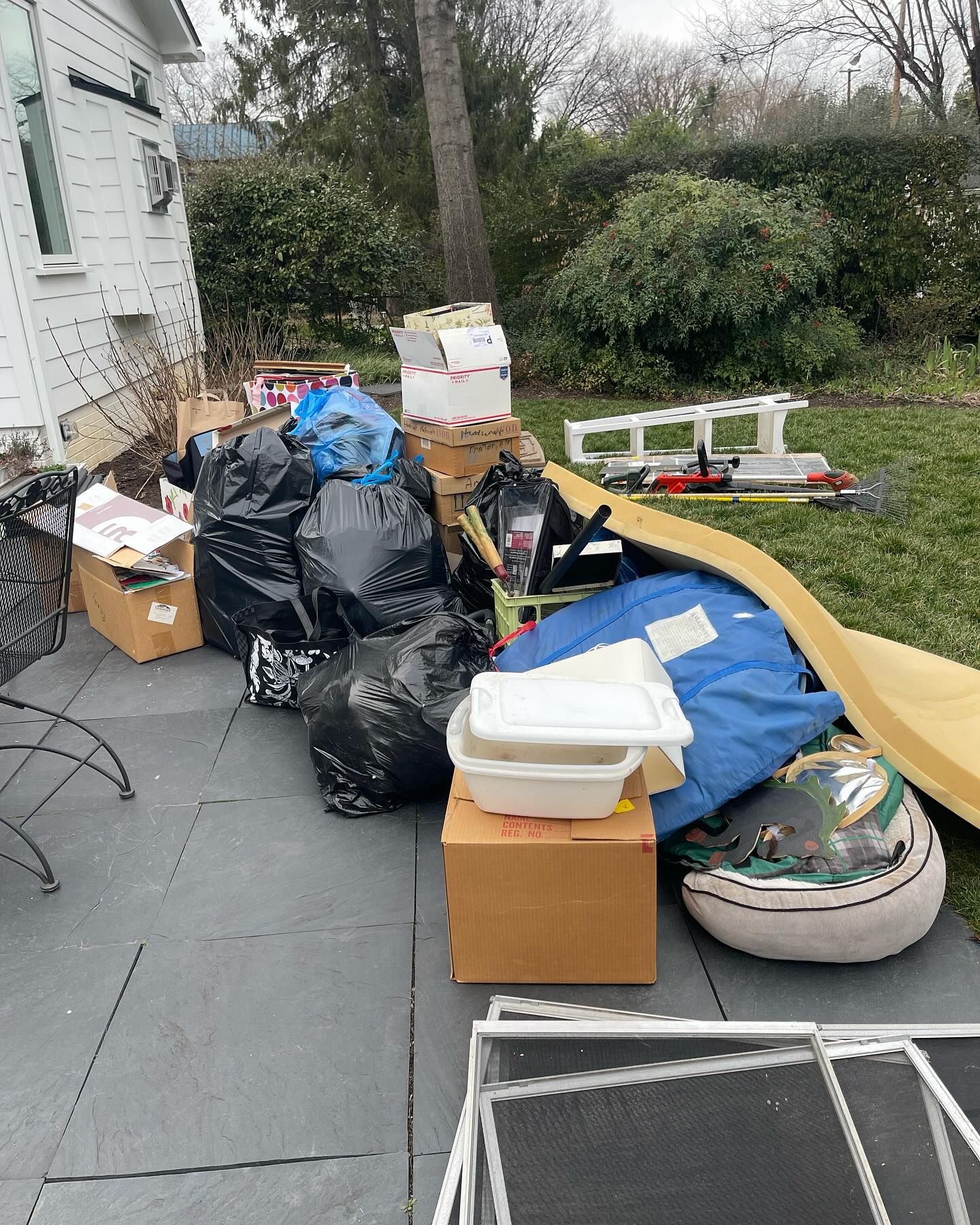 Pile of bags, boxes, and discarded items scattered on a patio beside a house.