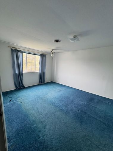 Empty room with blue carpet, white walls, and a window with blue curtains and blinds.