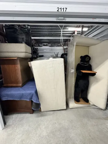 Packed storage unit with furniture stacked tightly and a person in black standing in the doorway