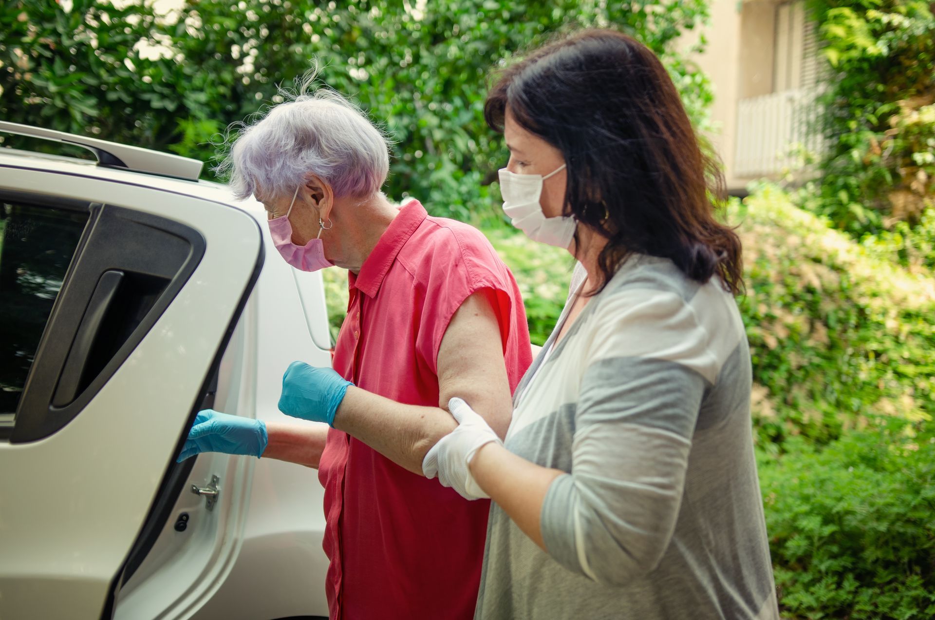 Two masked people loading supplies into a car outdoors, one wearing red and blue gloves.