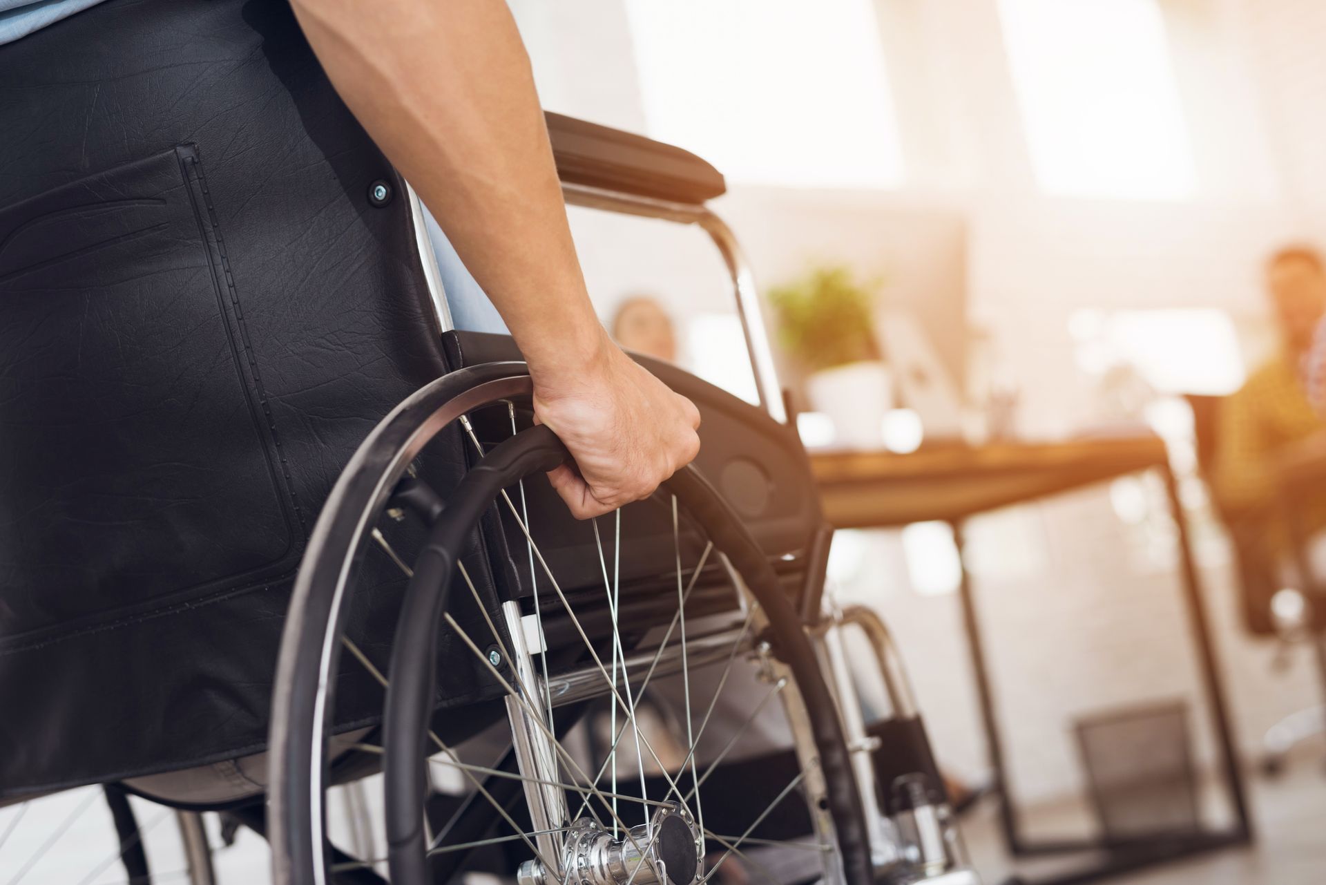 Person holding a wheelchair in a bright room near a table and chairs