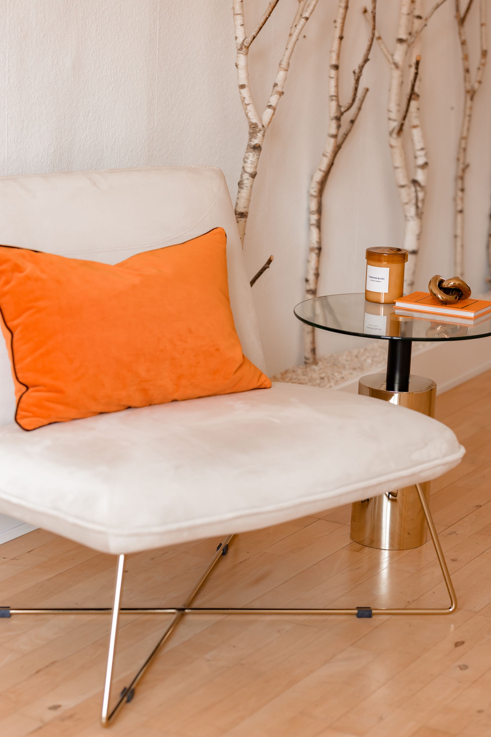 Ein weißer Stuhl mit einem orangefarbenen Kissen steht neben einem Glastisch