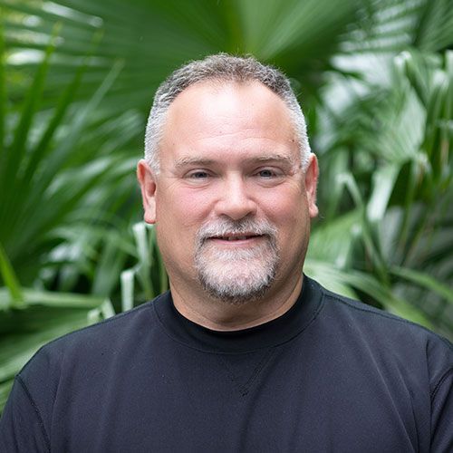 A man with a beard is wearing a black shirt and smiling for the camera.