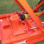 Orange brush hog mower deck with a yellow drive shaft and black coupling.
