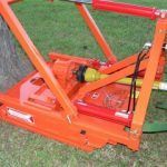 Orange farm equipment with a yellow drive shaft resting on green grass.