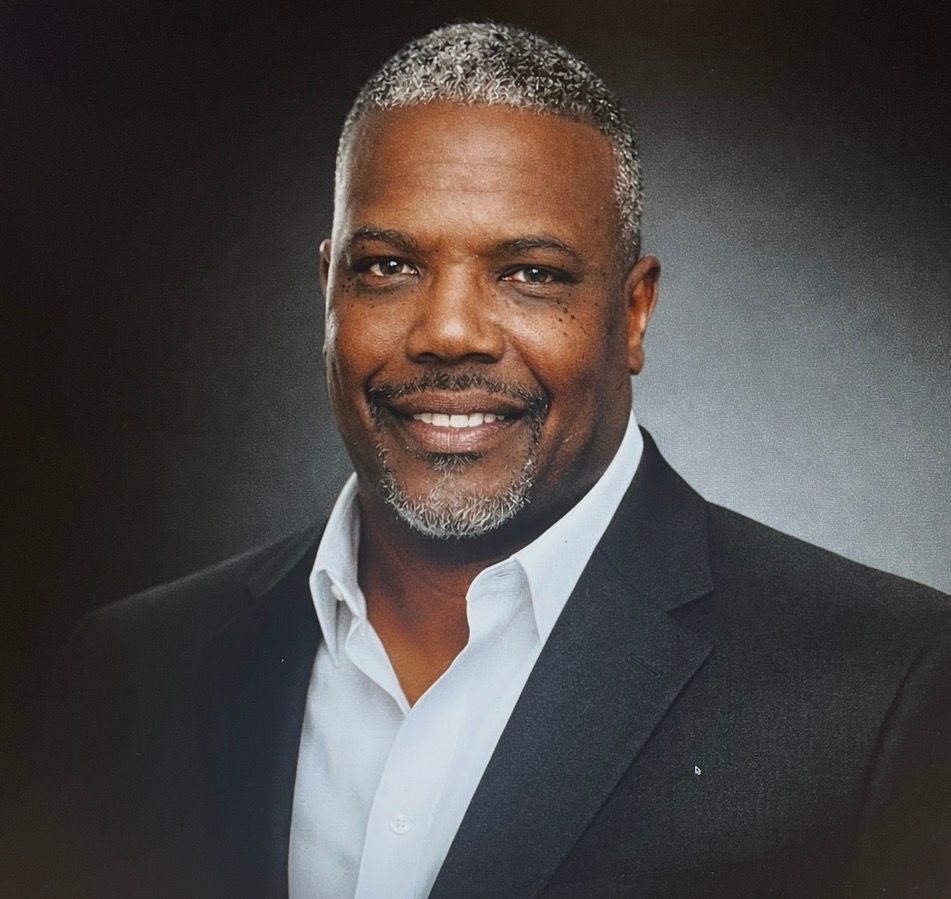 A woman is sitting at a desk with a laptop and a vase of flowers.