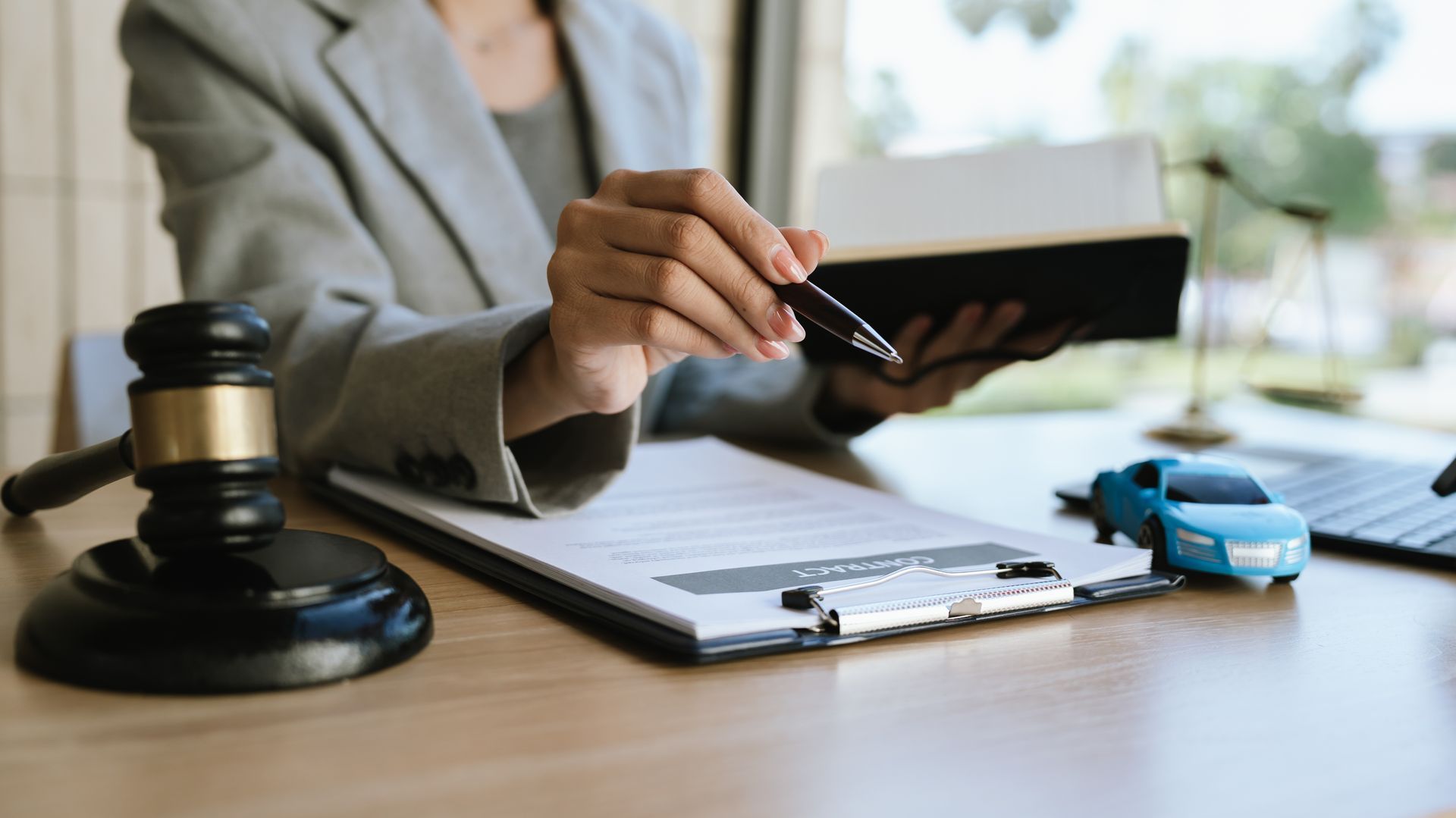 A lawyer signing a car contract with a gavel and a toy car on the desk.