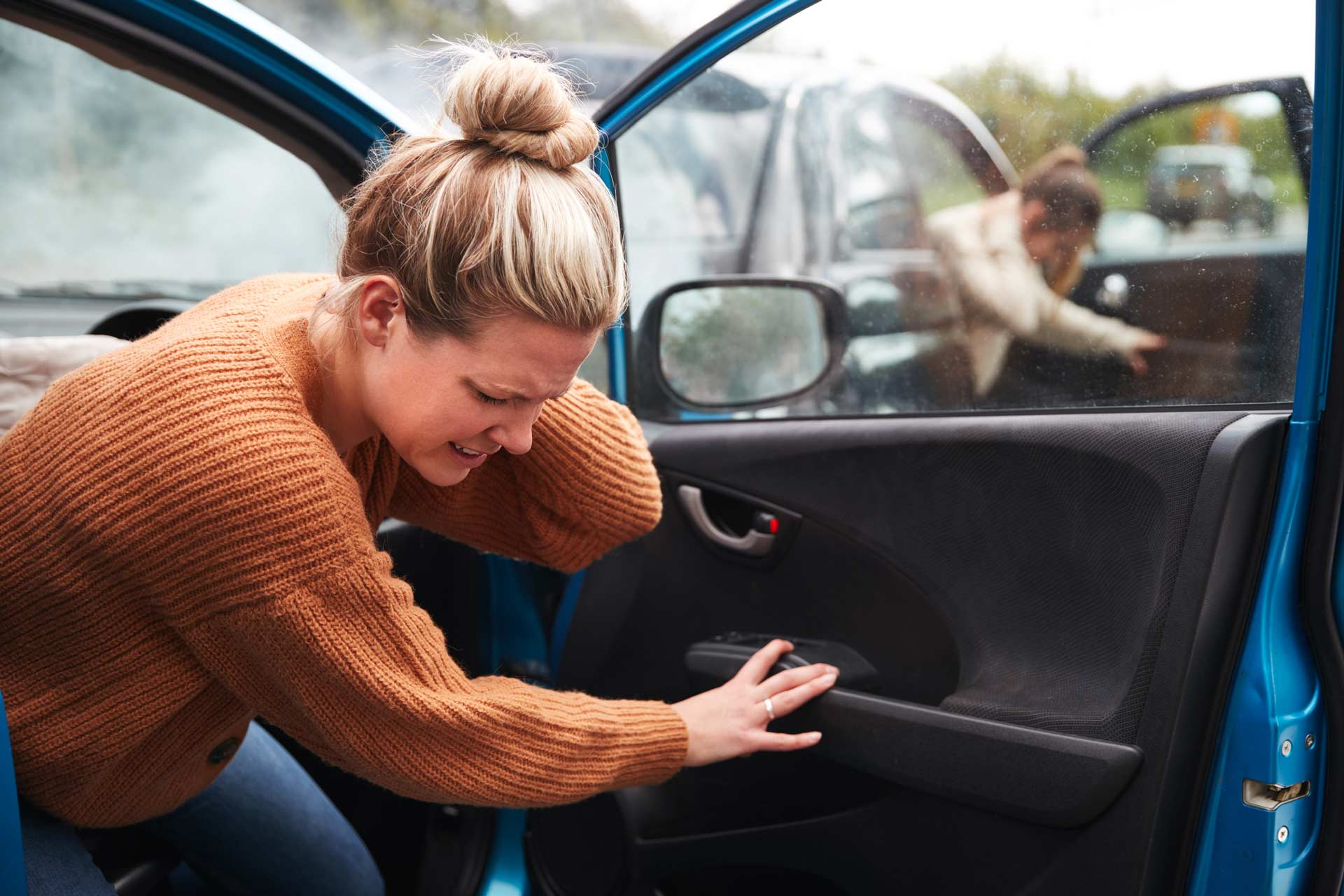 Woman exiting a blue car, looking distressed. Another person in a gray car is nearby. Woman exiting a blue car, looking distressed. Another person in a gray car is nearby.