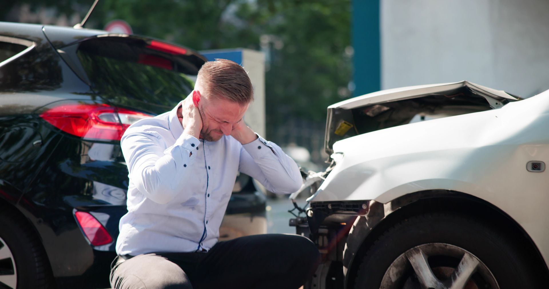 A white man with hands on his head kneels by damaged cars after a crash