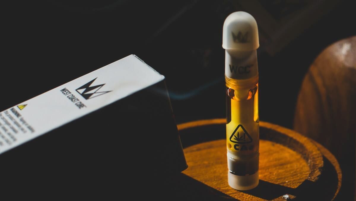 A vape pen is sitting on a wooden table next to a box.