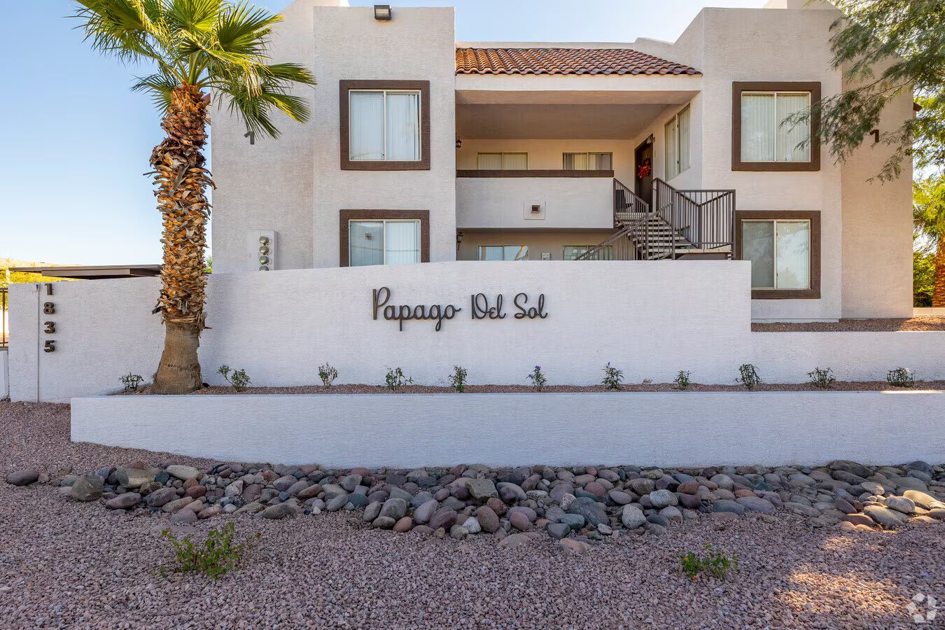 Photo of the apartment entrance showing the community sign and a few trees around the building