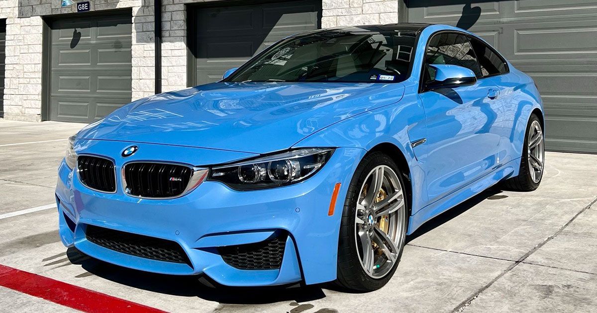 Bright blue BMW M4 coupe parked in front of garage doors.