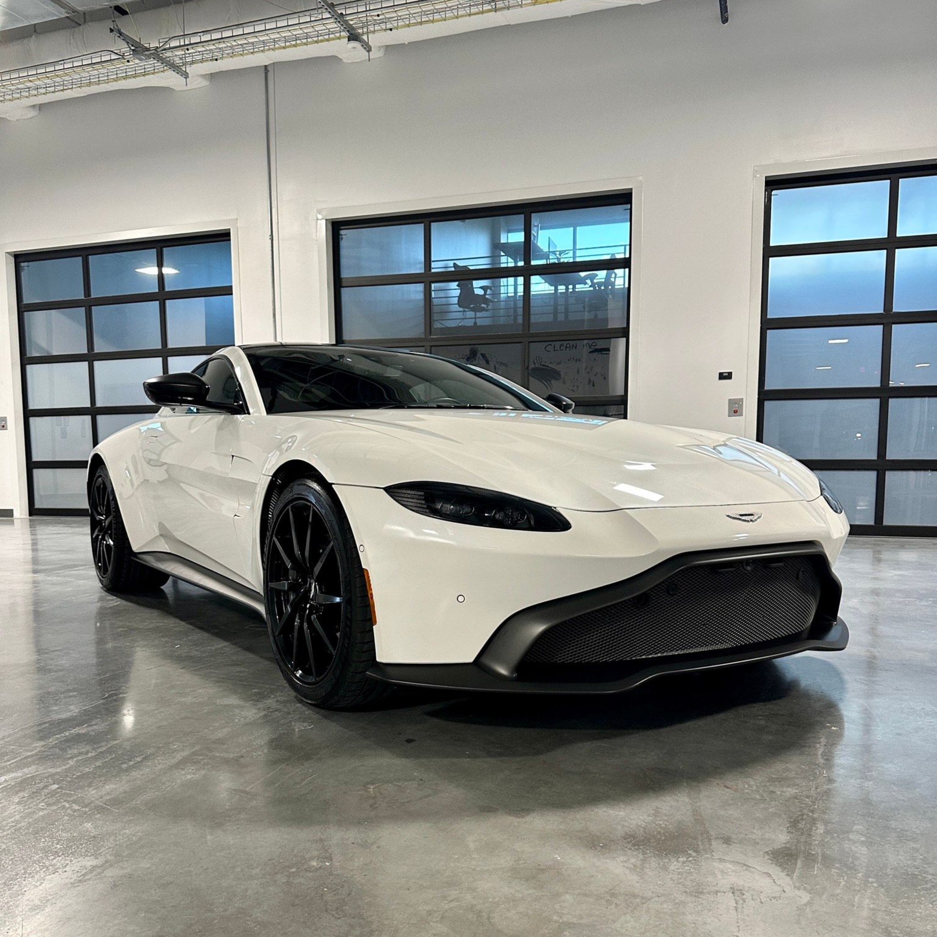White Aston Martin sports car parked inside a modern garage with large glass doors.