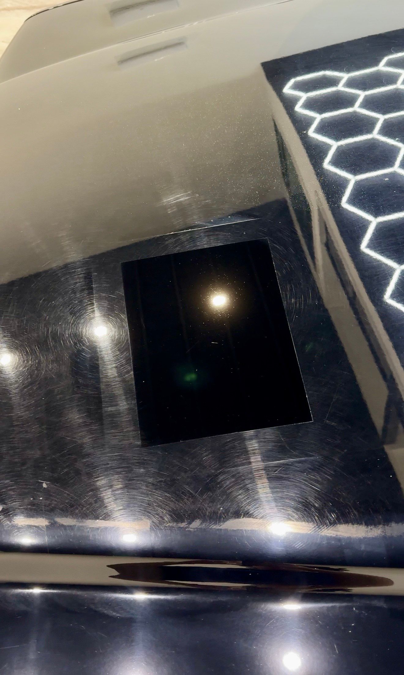 Black surface with a bright light in the center, a geometric pattern is visible to the right.