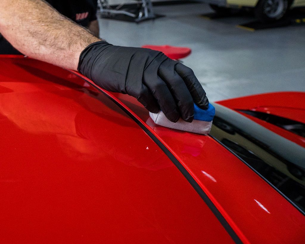 Gloved hand applying a ceramic coating to a black car surface, reflecting light.