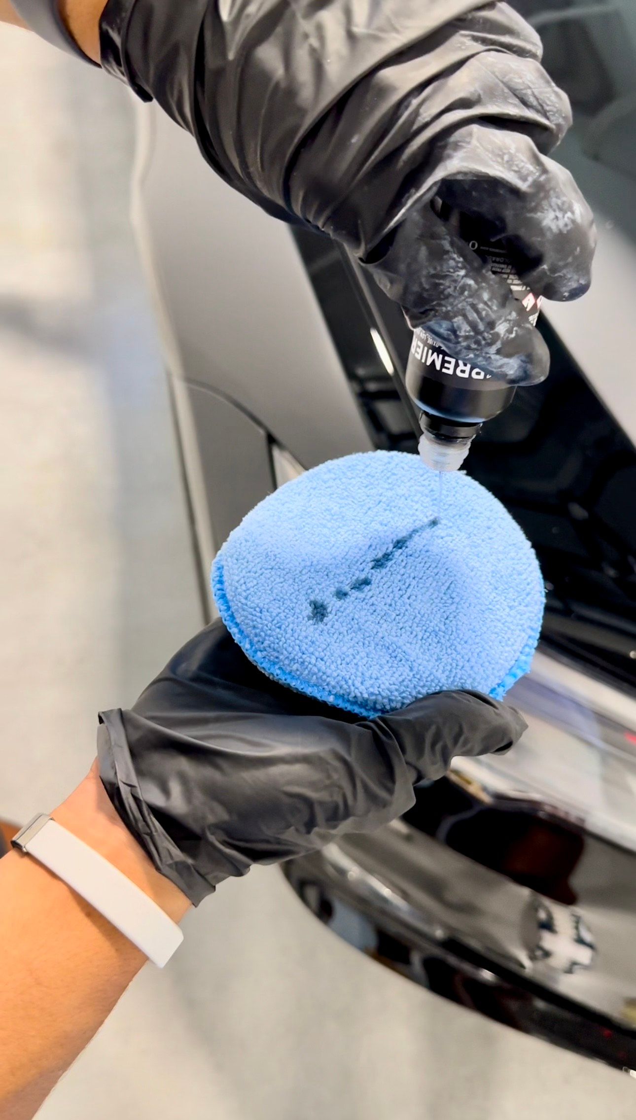 Hands in black gloves applying a blue pad to a shiny black car surface.